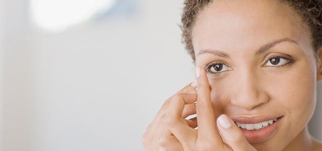 Une femme avec une lentille de contact sur son doigt sur le point de la poser sur son oeil 